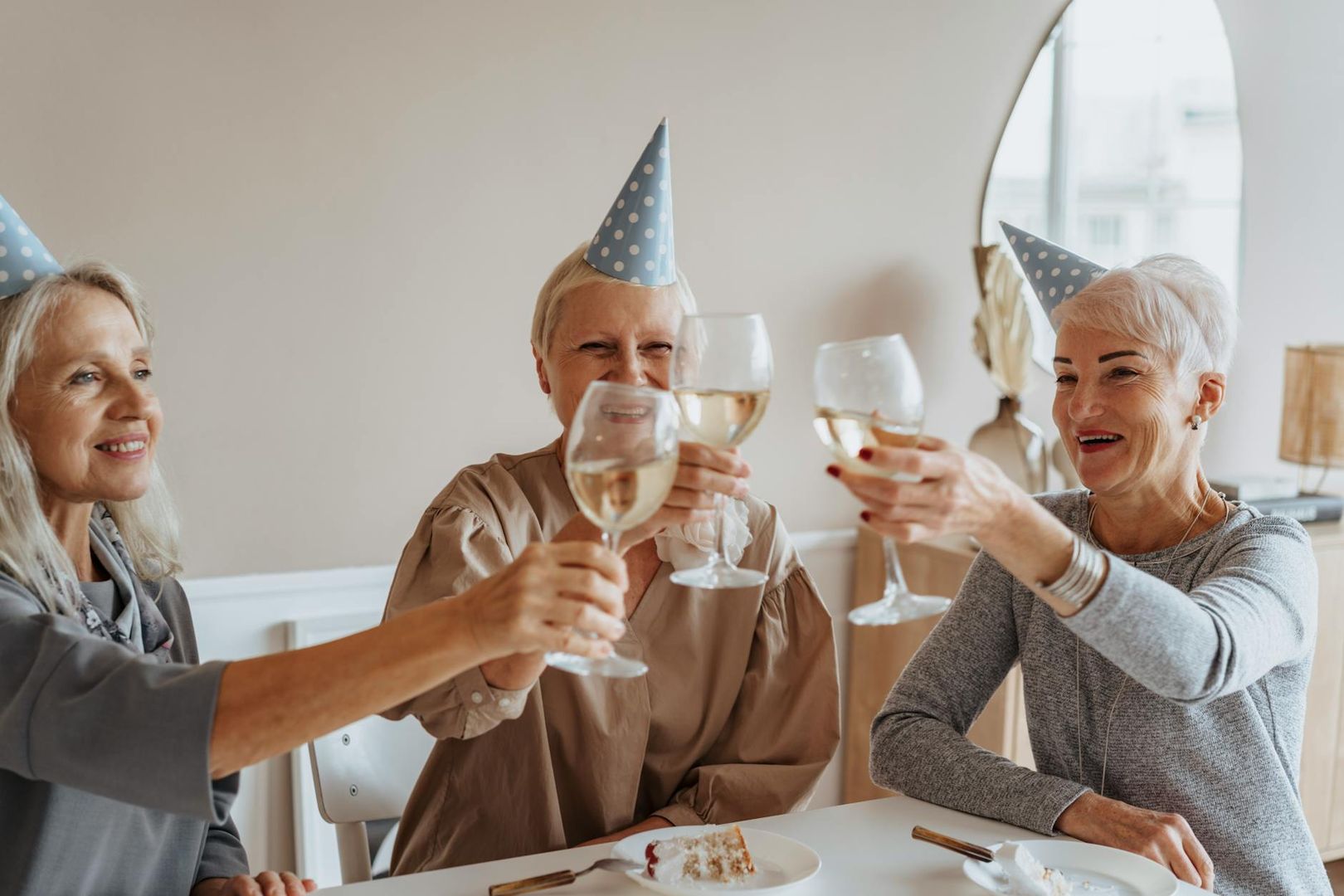 Tre glada kvinnor i kalashattar skålar med vin under ett firande.