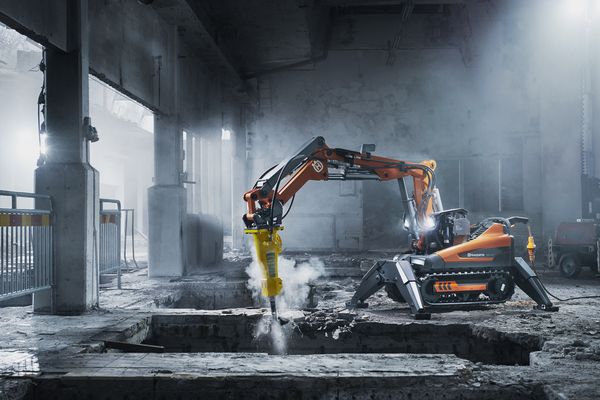 En orange och grå rivningsrobot arbetar i en dammig industrilokal.